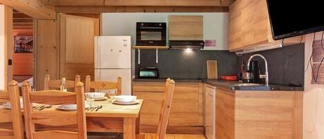 Una cocina compacta con armarios de madera, una mesa de comedor lista para cuatro comensales y un microondas empotrado.