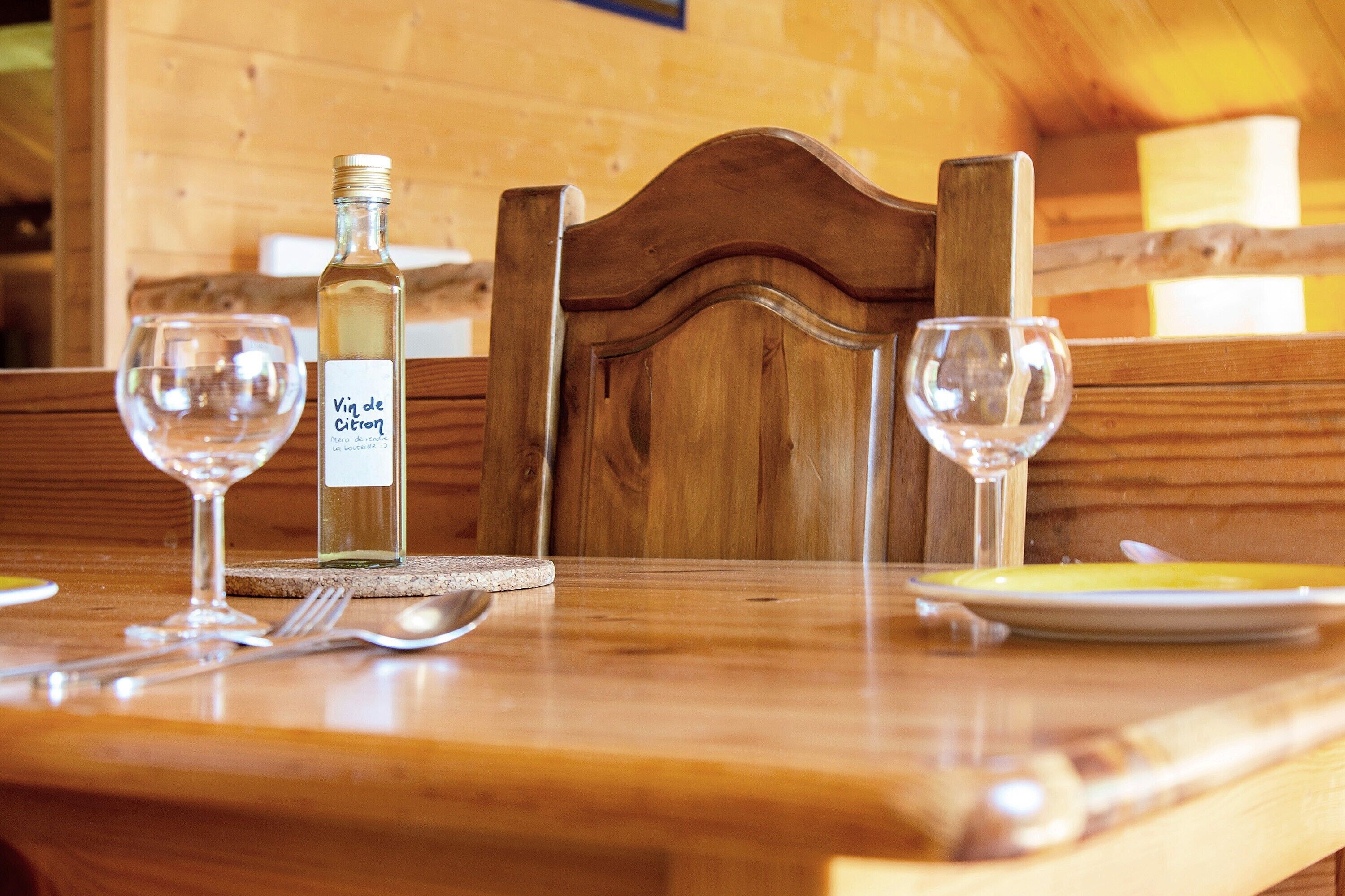 Ein Holztisch mit einer Flasche 'Vin de Citron' und zwei leeren Weingläsern.
