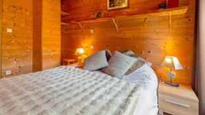 Una habitación de cabaña de madera con una cama, dos lámparas de noche, una estantería con libros y un cuadro en la pared.