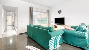 A modern living room with a sofa set, a flat-screen TV, and a window with curtains.