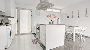 A modern kitchen with a built-in washing machine, a central island, and a dining area with white chairs.