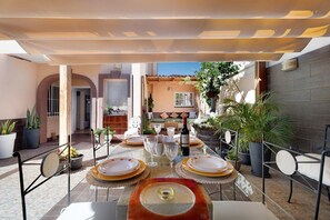 Un coin repas avec des tables dressées pour le repas, des plantes en pot et une bouteille de vin.