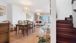 A dining area with a wooden table and chairs, a sofa, and a staircase leading to an upper floor. - Vacation Home 'Vitamina Village' with Sea View, Shared Pool, Garden & Wi-Fi (Adeje)