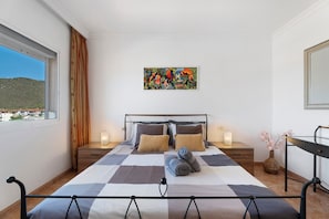 Une chambre à coucher avec un grand lit, deux tables de chevet, une commode, une fenêtre avec des rideaux, un tableau au mur et un miroir au mur.