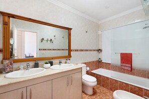 Une salle de bain avec deux lavabos, des toilettes, une baignoire et un grand miroir.