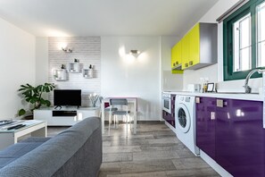 A modern kitchen with a washing machine, a dining area with a table and chairs, and a living area with a sofa.