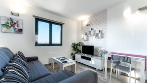 A modern living room with a sofa, a coffee table, a TV, and a desk with a chair.