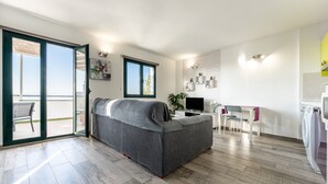 A modern apartment with a grey sofa, a dining table, a TV, and a balcony.