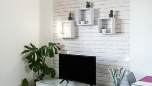 A modern living room with a flat-screen TV, white brick wall, and minimalist shelving with potted plants.