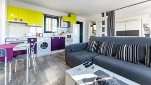 A compact living space with a kitchenette, a sofa, a dining area, and a washing machine.
