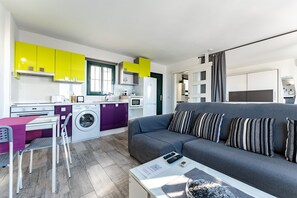 Un espace de vie compact comprenant un coin cuisine, un canapé, un coin repas et un lave-linge.
