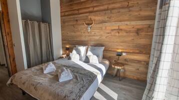 Een slaapkamer met een houten wand, een bed met witte beddengoed, twee nachtkastjes met lampen, en een hertenhoofd aan de muur.