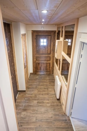 Un pasillo estrecho con suelo de madera, una puerta de madera al final y un radiador blanco a la derecha.