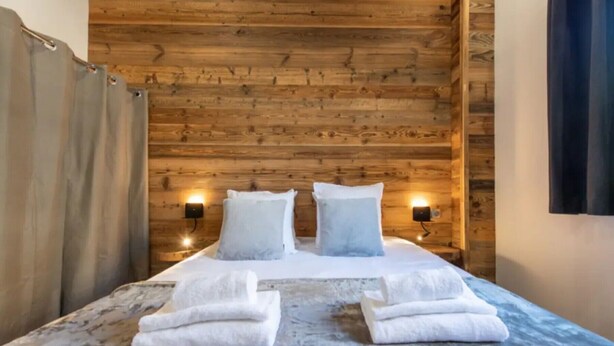 Ein holzgetäfeltes Zimmer im Blockhausstil mit einem Bett, zwei Wandleuchten und einem Vorhang.