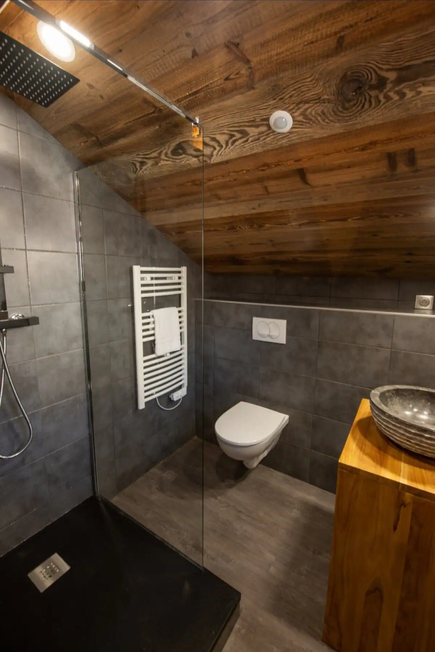 A modern bathroom with a shower, toilet, and a wooden vanity with a bowl sink.