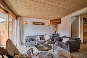 Una sala de estar acogedora con techo de madera, un conjunto de sofás, una chimenea y un ventanal grande.