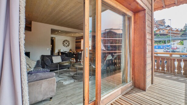 Une terrasse en bois avec une porte vitrée donnant sur un espace de vie comprenant un canapé et une table basse.