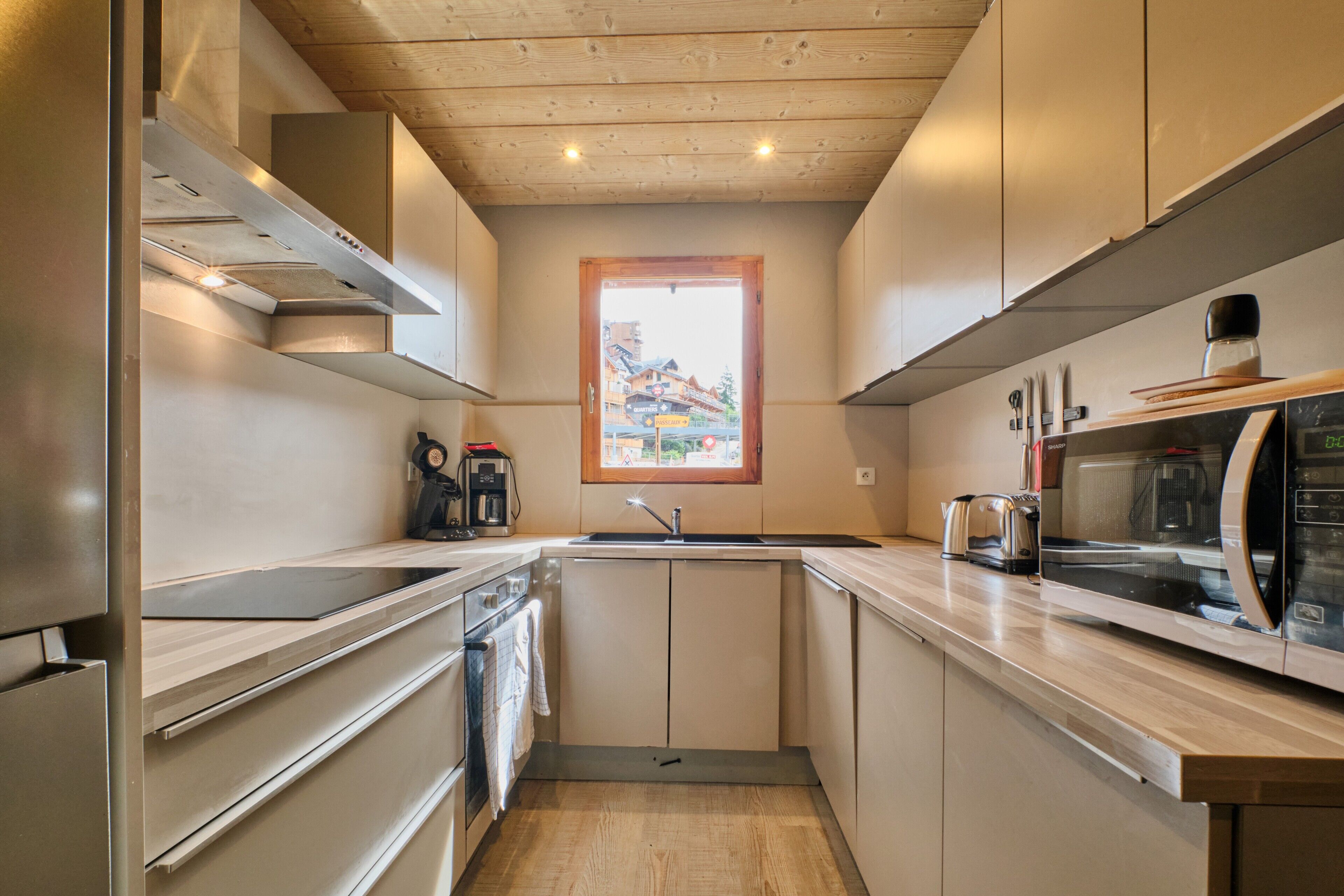Une cuisine compacte avec un plafond en bois, des appareils électroménagers intégrés et une fenêtre donnant sur des immeubles.