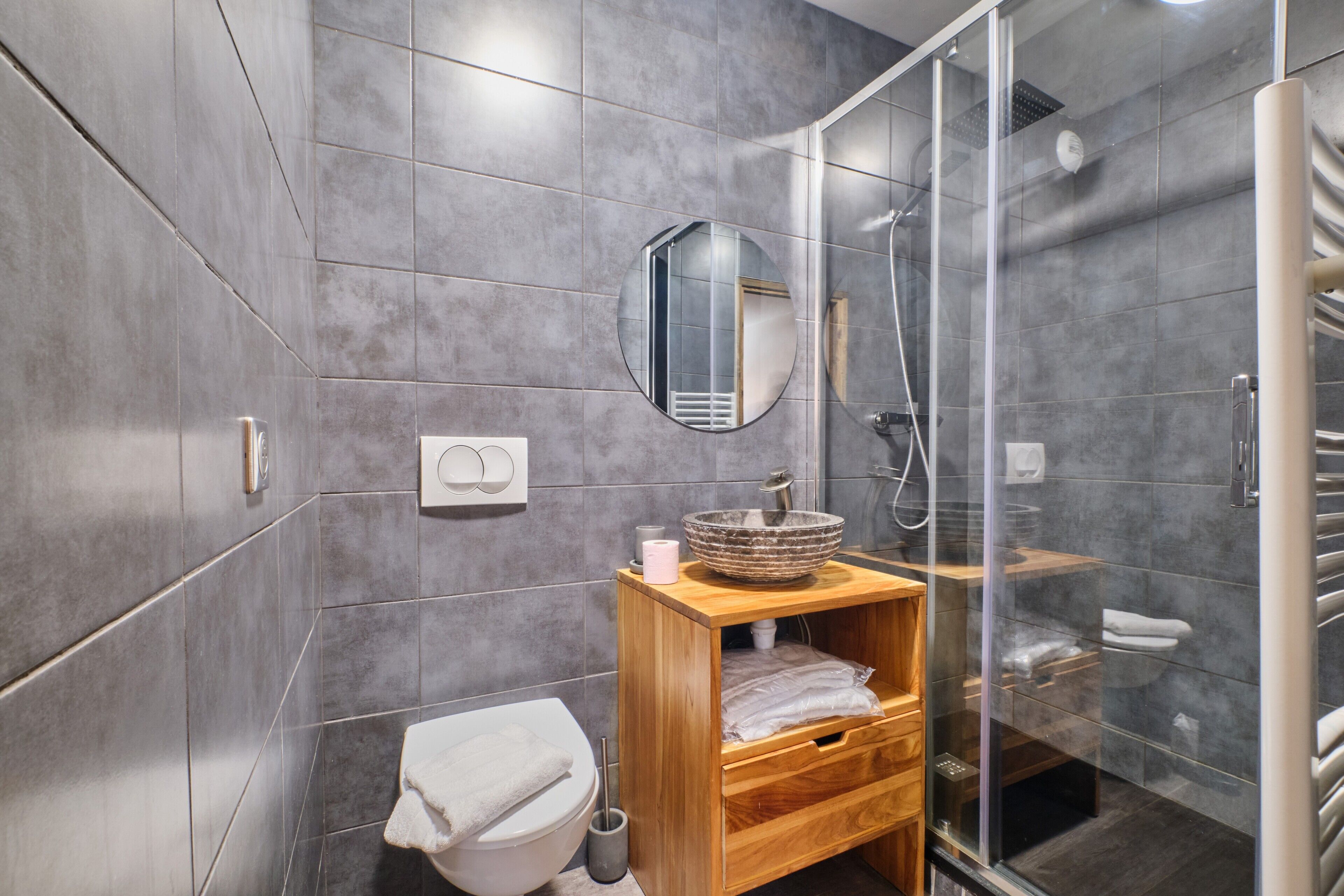 Un bagno moderno con box doccia in vetro, mobile bagno in legno con lavabo a incasso e water con coperchio bianco.