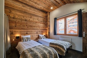 Una habitación con paredes de madera, dos camas con ropa blanca, una ventana con cortinas y un radiador.