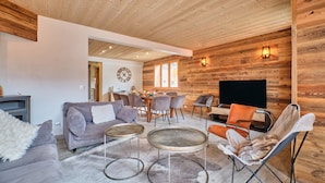 Un salon chaleureux avec un plafond en bois, une cheminée, un coin repas et un téléviseur.