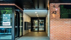 A modern building entrance with a glass door, a 'For Lease' sign, and a neon sign for 'M. Forty Two'.