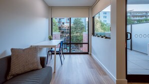 A modern room with a sofa, a small table, and a chair. It has large windows offering a view of buildings and trees outside.