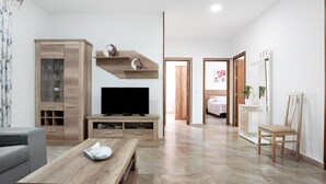 Un salon moderne doté d’un téléviseur à écran plat, de meubles en bois, d’un canapé gris et d’un coin repas.