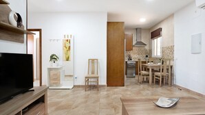 Un salon moderne avec un téléviseur, un coin repas avec une table et des chaises, et une cuisine en arrière-plan.