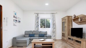 Un salon avec un canapé gris, une table basse en bois, un téléviseur posé sur un meuble en bois et une fenêtre avec des rideaux.