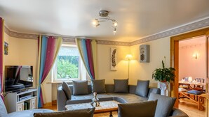 Una sala de estar con un conjunto de sofás, una televisión, una lámpara y un comedor con mesa y sillas.