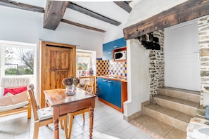 Une cuisine avec des meubles de rangement bleus, une table à manger en bois et un mur en pierre.
