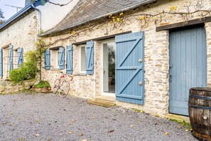 A stone building with blue shutters, a bicycle, and a barrel.