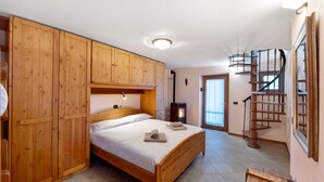 Un dormitorio con cama de madera, armario empotrado, banco de madera, escalera de caracol y estufa de leña.