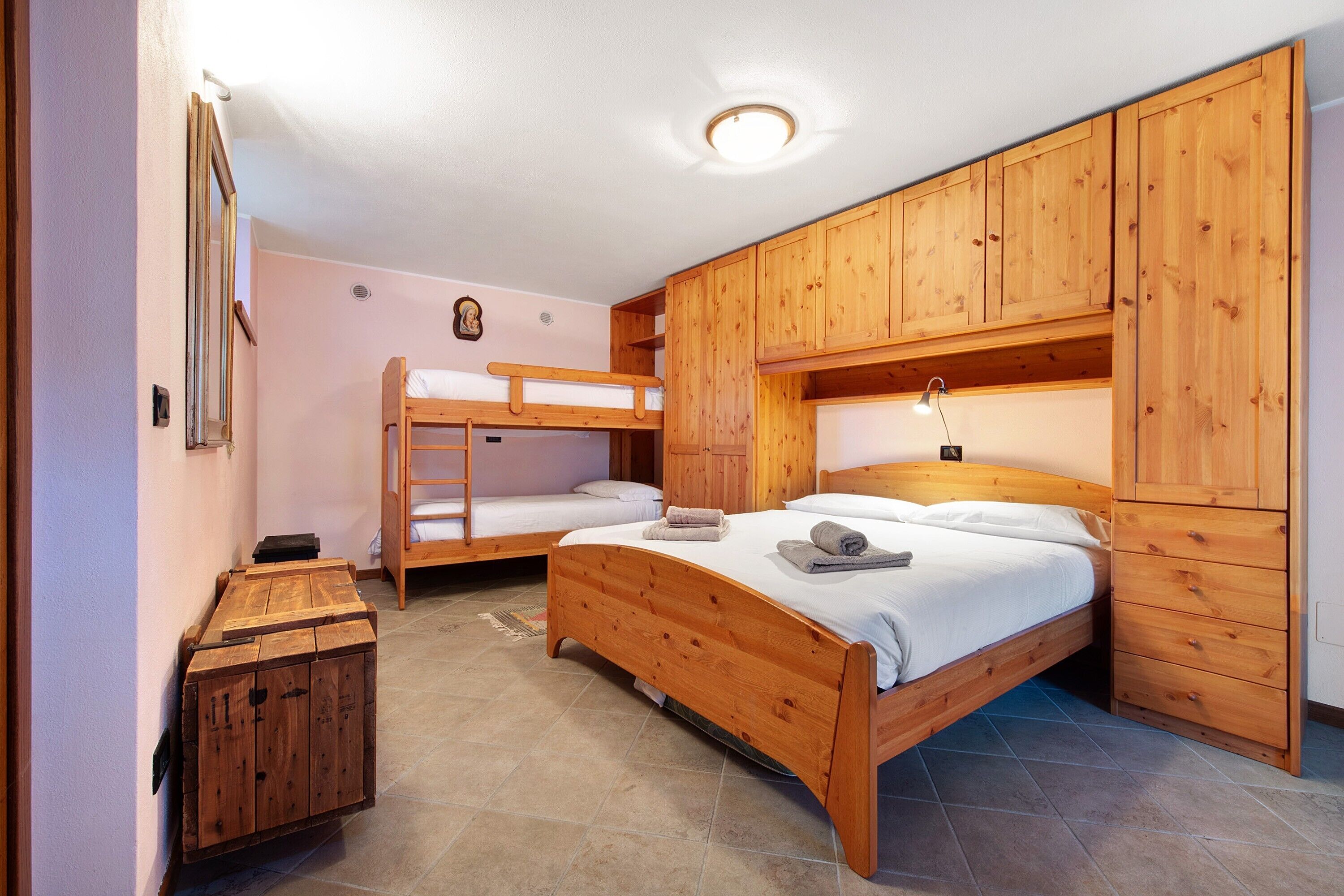 A room with two bunk beds, wooden cabinets, a small wooden chest, and a ceiling light.