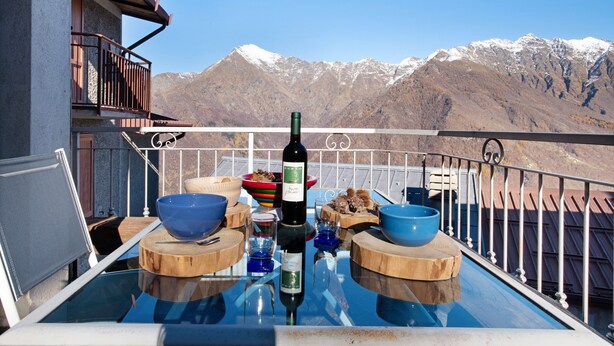 Un balcón con una mesa dispuesta para cenar, una botella de vino y cuencos.