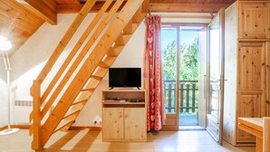 A wooden staircase leading to a balcony with a TV on a wooden cabinet. - Apartment 'Appartement 8' with Mountain Views, Shared Garden and Wi-Fi (Saint-Sorlin-d'Arves)