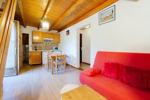 A kitchen with wooden cabinets, a dining table with chairs, a red sofa, and a chandelier.