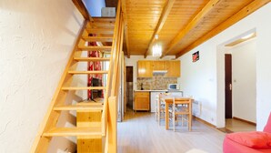 A wooden staircase leading to a loft bedroom, a kitchen with wooden cabinets, and a living area with a red sofa. - Apartment 'Appartement 8' with Mountain Views, Shared Garden and Wi-Fi (Saint-Sorlin-d'Arves)