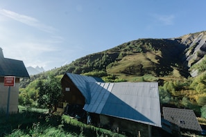 Un bâtiment rustique, doté d’un toit en tôle ondulée, entouré d’une végétation luxuriante et avec des montagnes en arrière-plan.