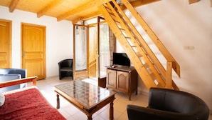 Una habitación con techo de madera, una cama, una mesa, un televisor sobre un mueble de madera y una silla.