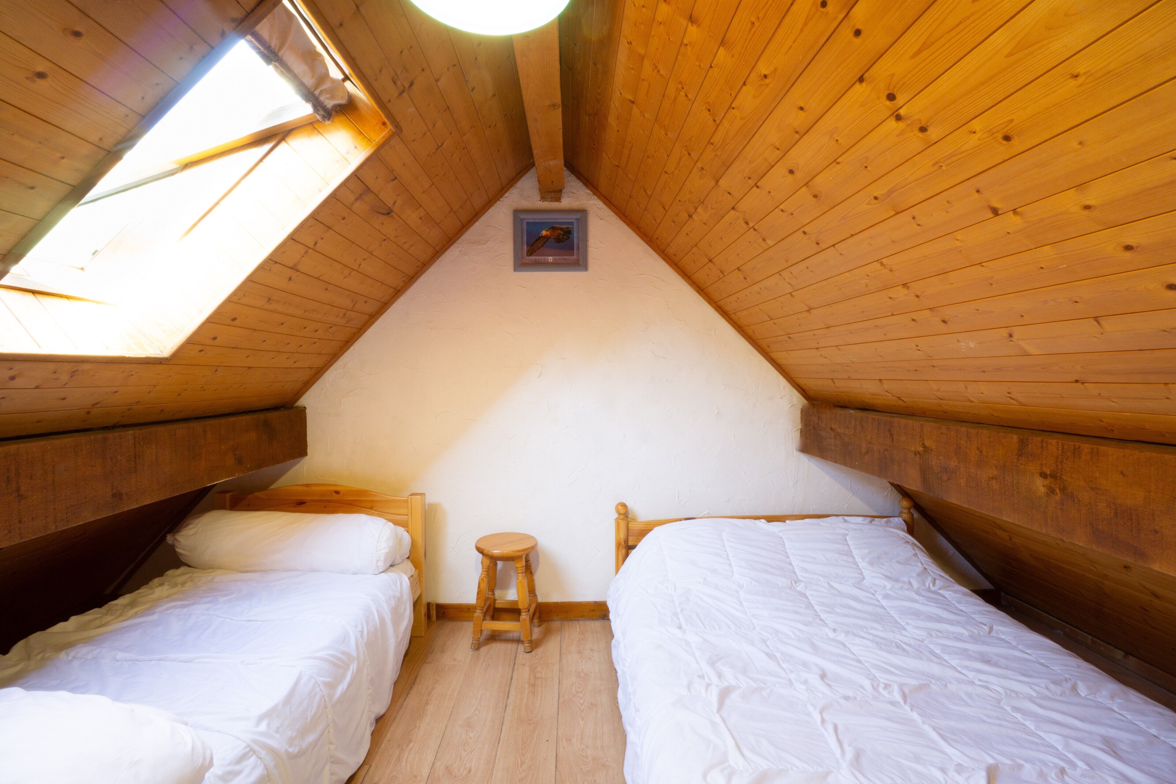 Una piccola stanza in legno con due letti, uno sgabello e un lucernario.