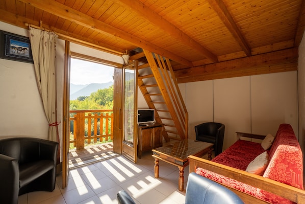 A wooden interior with a balcony, a TV, and a sofa.