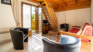Una habitación con techo de madera, una escalera, un televisor, un sofá y una silla.