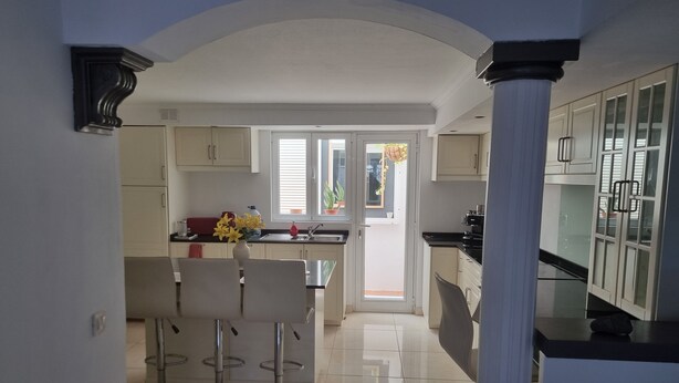 A modern kitchen with a central island, bar stools, and a view through a glass door to an outdoor area.