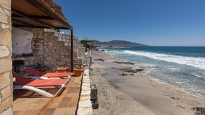 A beachside hotel with stone walls, red lounge chairs, and a view of the ocean. - Vacation Home 'Casa Nostra' with Sea View, Terrace & Wi-Fi (Pájara)