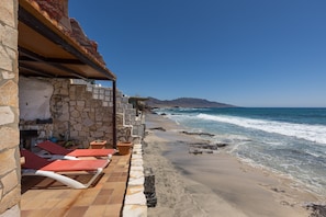 Ein Hotel am Strand mit Steinmauern, roten Liegestühlen und Blick auf den Ozean.
