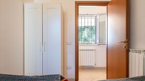 A room with two beds, a wardrobe, a radiator, and a window with a view of greenery.