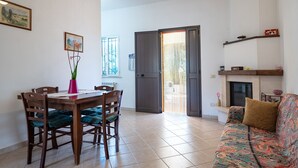 A dining area with a wooden table and chairs, a vase with flowers, and a sofa with a patterned throw.