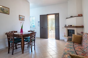 A dining area with a wooden table and chairs, a vase with flowers, and a sofa with a patterned throw.